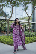 Woman in a pink traditional outfit standing outdoors with greenery in the background