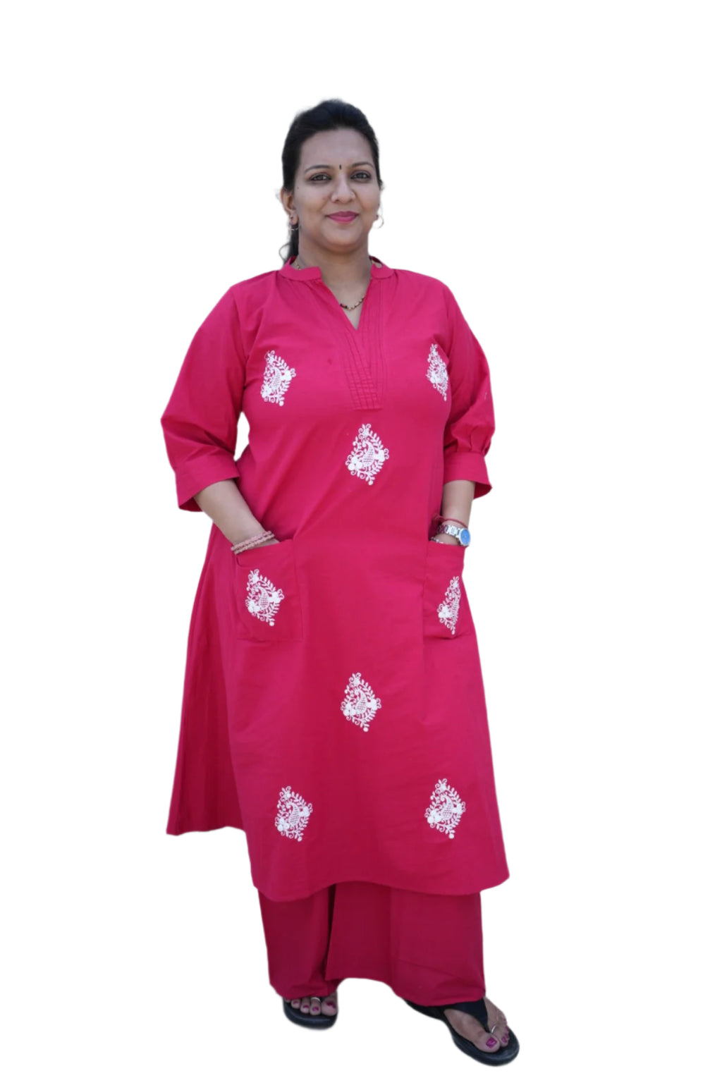 Woman wearing a bright pink traditional outfit with white patterns in a room with light-colored walls and a window.