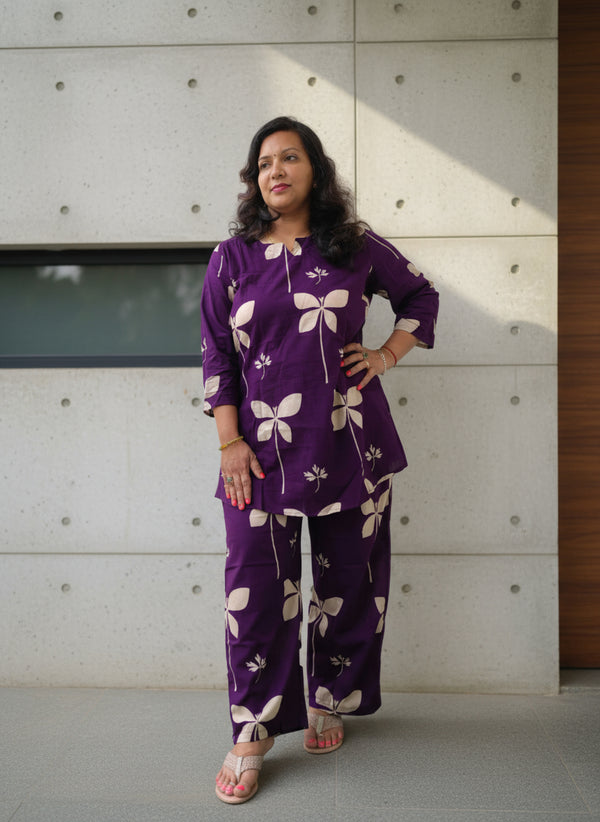 Person wearing a purple floral outfit standing indoors with a green carpeted floor.