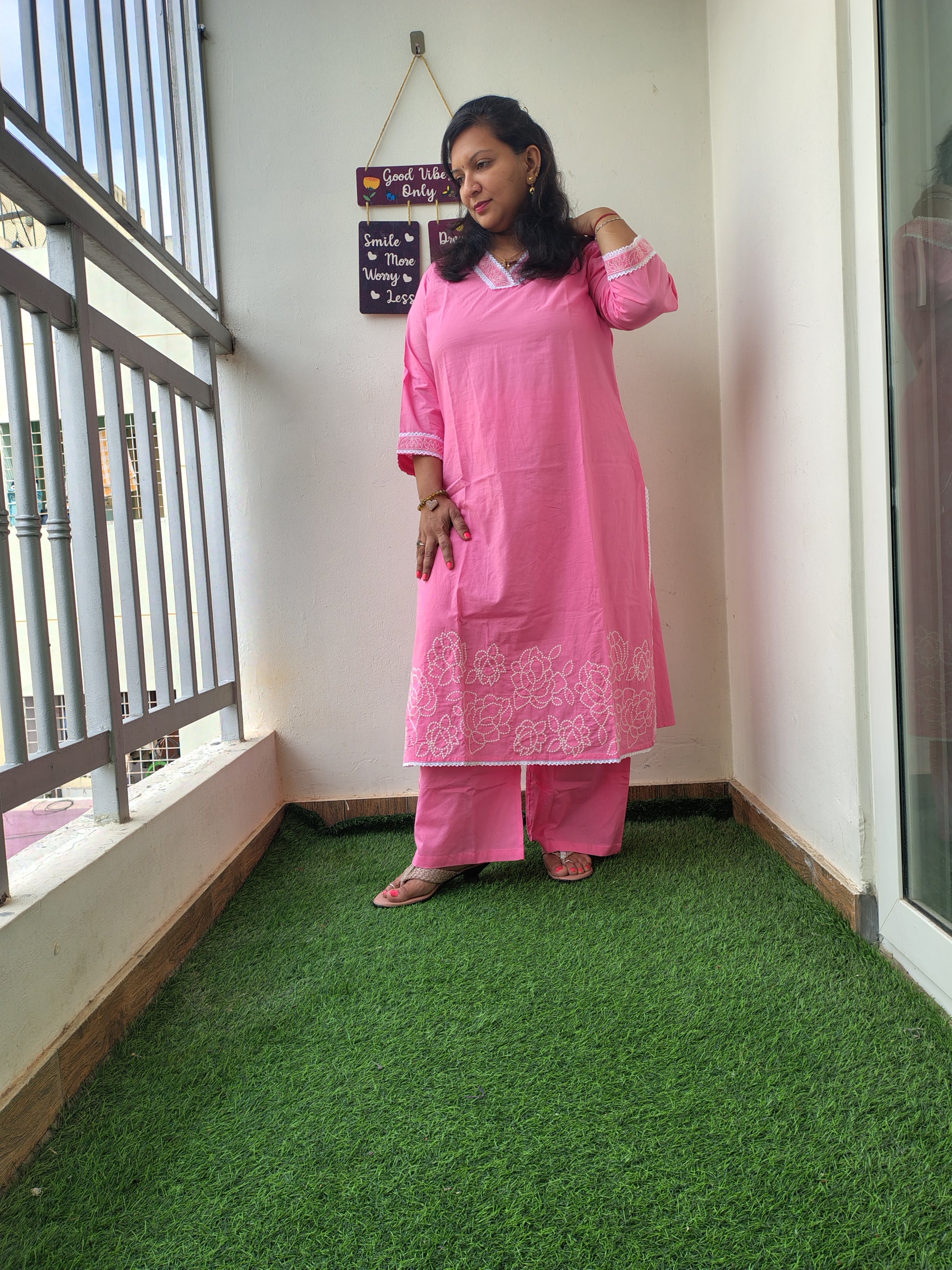 Person wearing a pink traditional outfit standing on artificial grass next to a white wall.