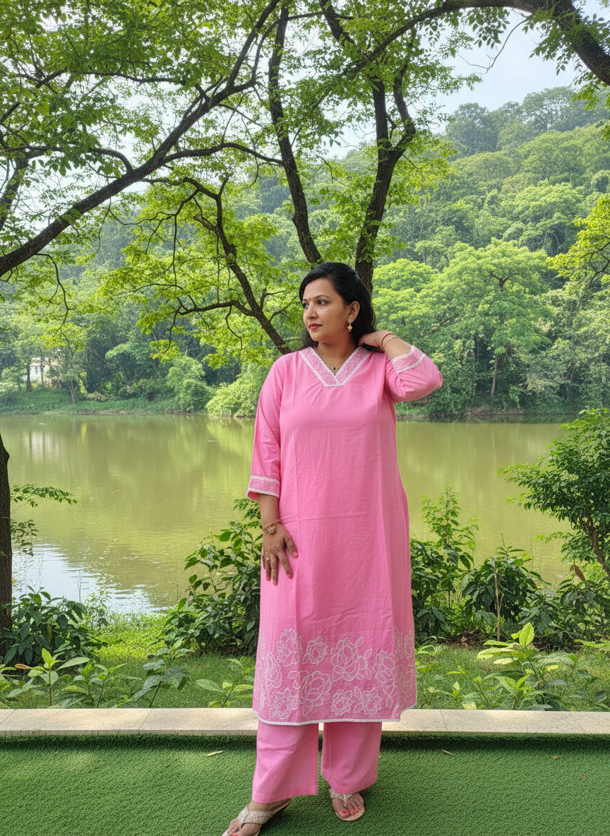 Person wearing a pink traditional outfit standing on artificial grass next to a white wall.