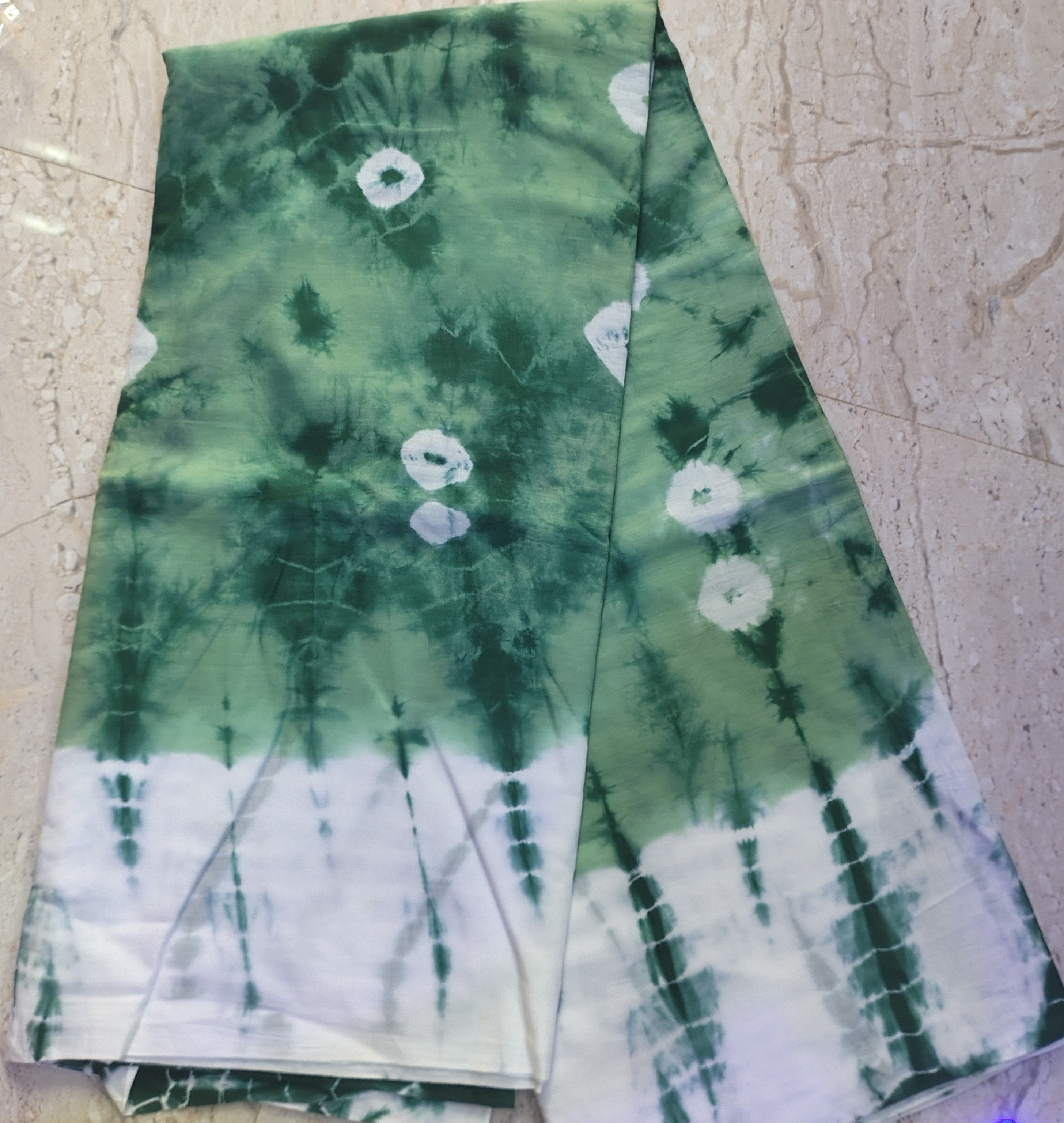Green and white tie-dye fabric on a textured surface